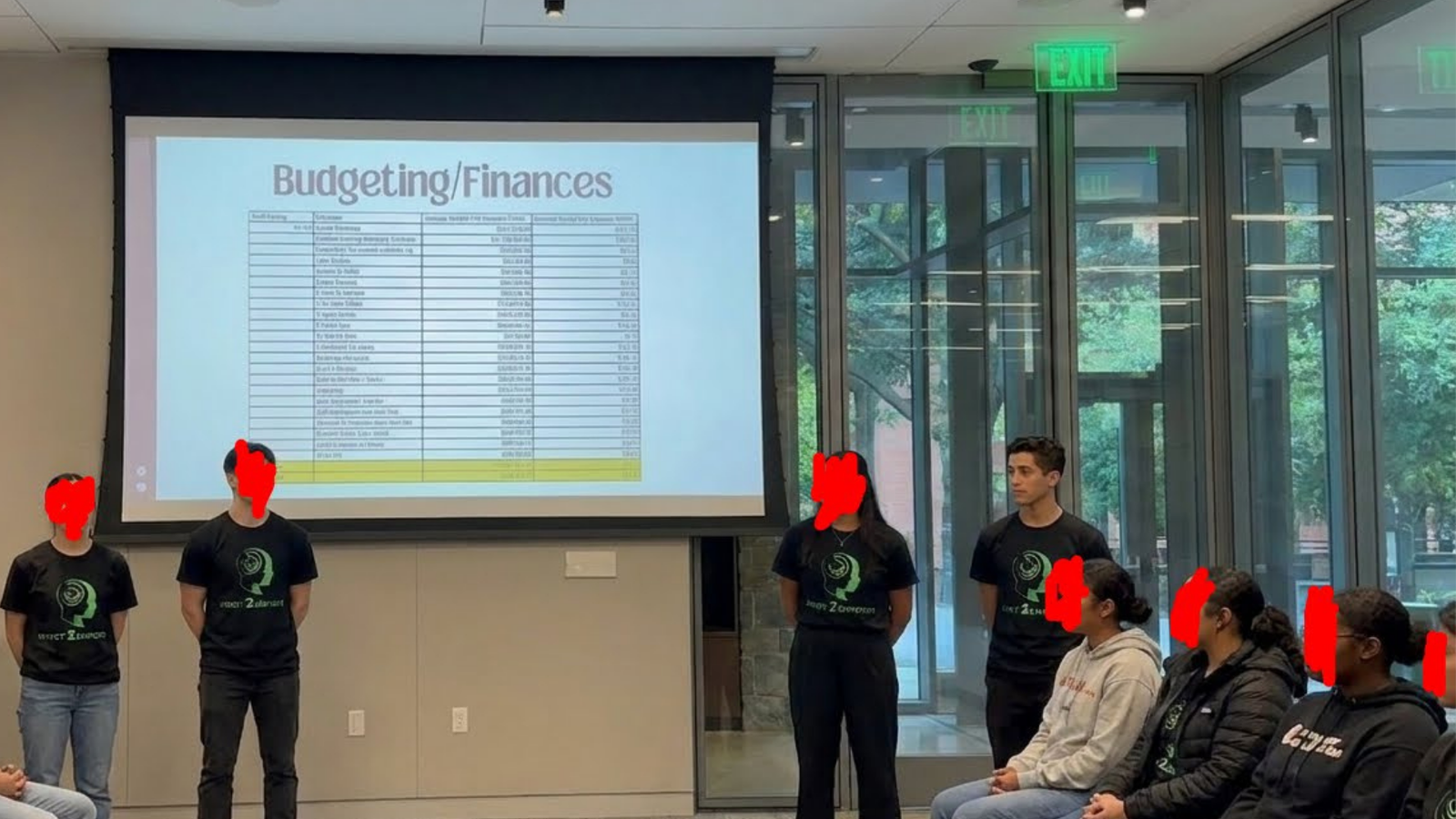 Invest2Empower team in branded shirts presenting a budgeting and finances worksheet to a seated group